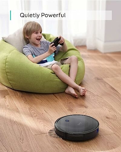 Child playing video games on bean bag with robot vacuum on floor.