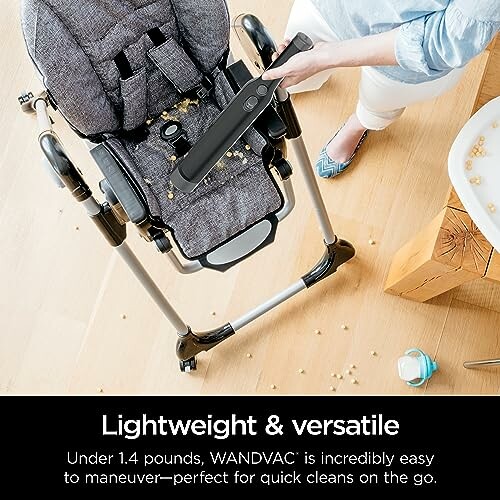 Person using handheld vacuum on high chair with spilled cereal.