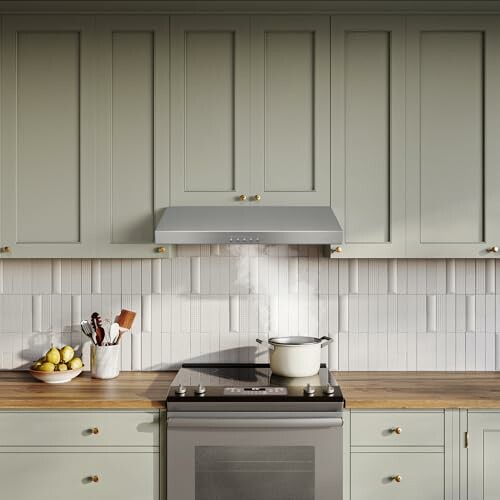 Modern kitchen with green cabinets, stove, and wooden countertops.